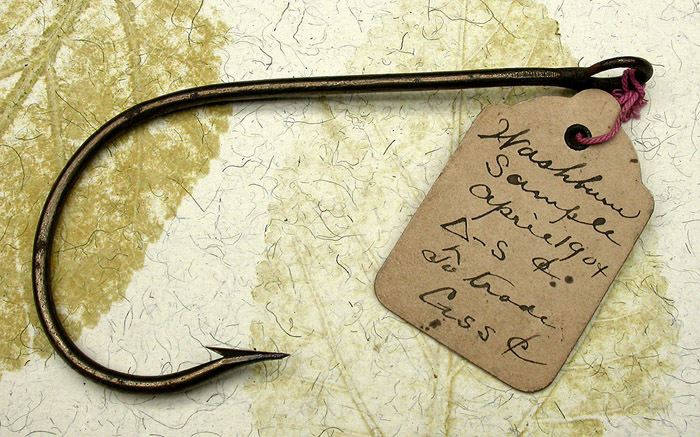 32a Washburn, sample hook, 13/0, hand formed tapered, welded ring eye, bronzed, ca 1904. The eye on this hook is very big, you could put a ¼” rope through it. The hand filing is great. You can imagine the hook maker filing the wire to a very fine taper and then bending it, what looks to me to be freehand. I have three of these hooks that are all slightly different. The original tag reads, Washburn, Sample, April 1904, a triangle-S &, to trade, C or G ss and the cents symbol. Were these prototype hooks? I don’t recognize the name. There’s a story there that we are unlikely to know. 1900’s collection.